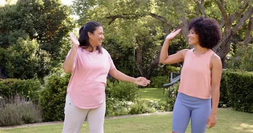 High-fiving, mother and adult daughter enjoying outdoor exercise in park, smiling and bonding