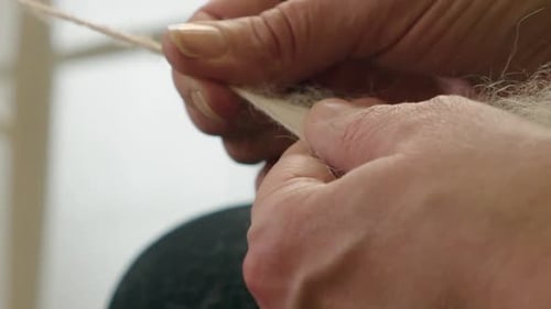 Closeup hands pull natural wool into spinning wheel, making grey yarn