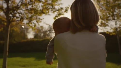 Mother walks in the park with her sleepy baby cradled in her arms