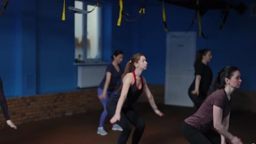 Un groupe de femmes en tenue de sport fait des exercices de respiration en s'accroupissant et en levant les bras