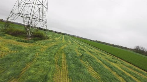 Freshly mown lawn grass in cultivation field beside transmission tower at cloudy day. Rural suburb a