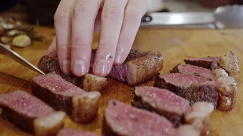 Cutting fried steak into pieces on a wooden cut board with a steel knife. Close up. Homemade cooking
