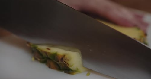Sharp Knife Cutting a Pineapple Slice on Board
