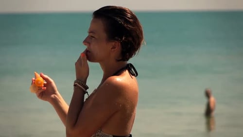 Young woman applies sunscreen to her face standing on a beautiful beach