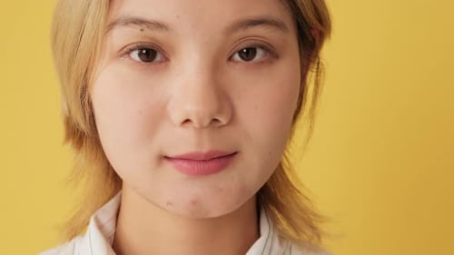 Portrait of young woman looking at camera with smile isolated on yellow background in studio