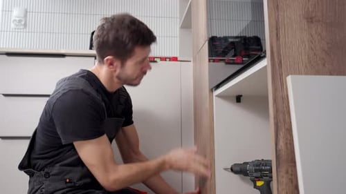 Handyman Fitting Kitchen Cabinet Panel During Installation