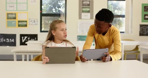 Diverse teenage classmates reacting as boy leaning in showing tablet at school desk, collaborating