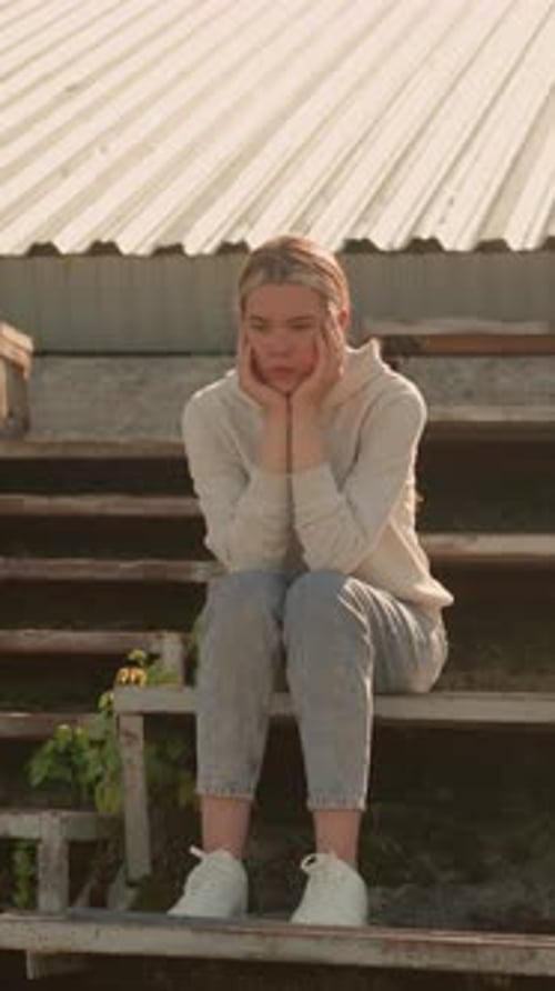 Pensive Woman in Hoodie Sitting on Rustic Stadium Bleachers