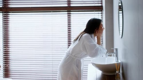 Woman in Robe Washing Face in Modern Bathroom