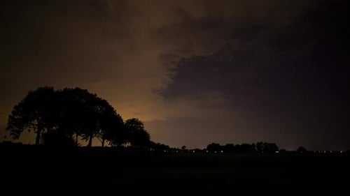 Beautiful time lapse of clouds passing behind the silhouette of trees at night on a quiet rural road