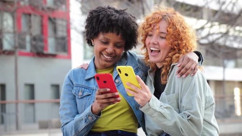 Two young women smiling, looking at mobile phones
