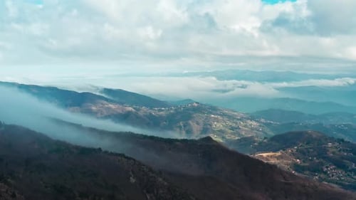 Misty mountain landscape with sunlit valleys and cloud-covered peaks, aerial view