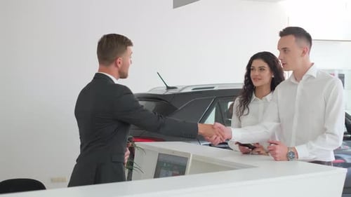 Happy Couple with Dealer Shaking Hands in Car Dealership