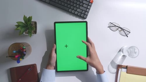 Top down view of man's hands using a mock up green screen tablet on white desk