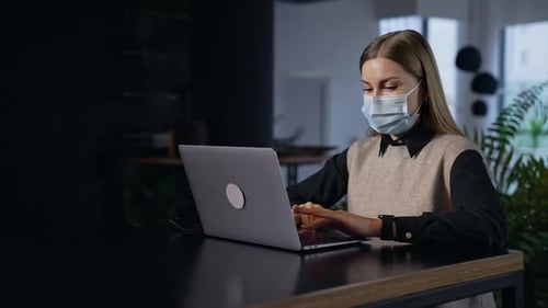 Woman Working on Laptop in Modern Office Wearing Mask