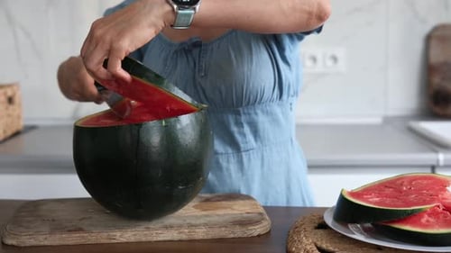 Woman Slicing the Top Off a Ripe Watermelon in Kitchen