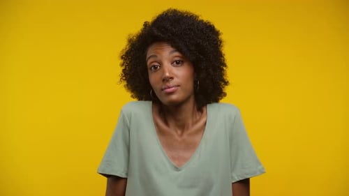 Woman Shrugs Shoulders in Front of Yellow Background