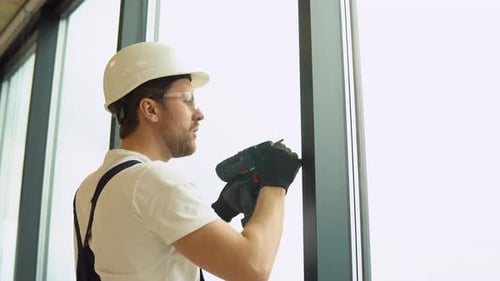 A Repairman in Uniform with Electric Screwdriver Fixing Pvc Windows in New Office