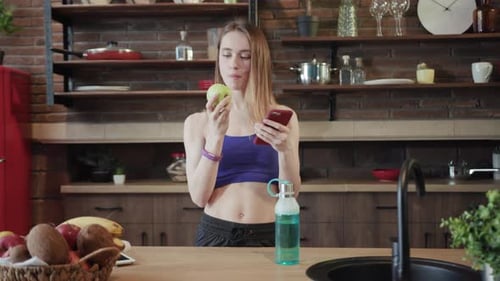 Young Woman Eating an Apple and Using Phone