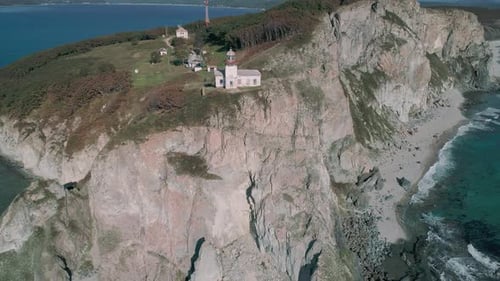 Aerial Panoramic View of White Lighthouse on the Rocky Cliff at Seaside Waves are Crashing to the