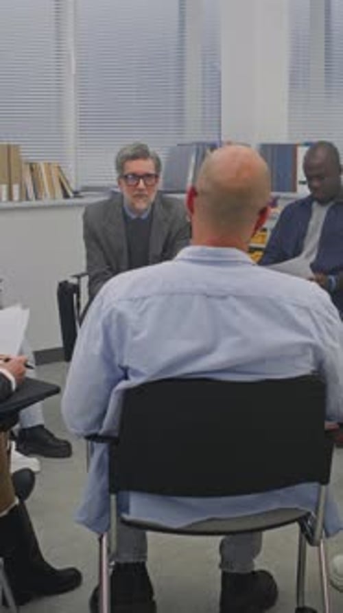 In Classroom With Large Windows and Chalkboard Schedule on Wall Circle Adult Learners Listens