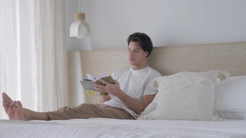 Young Man Relaxing Reading Book on Bed
