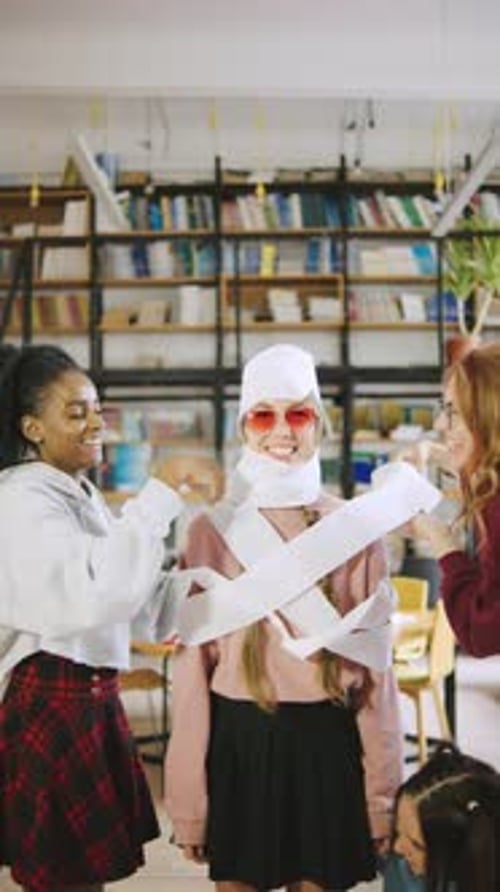 Friends Enjoying a Playful Moment in a Library While Wrapping One of Them in Toilet Paper During a