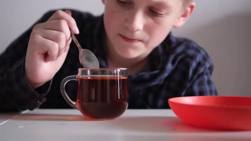 Boy Stirs Tea with Spoon in Clear Mug