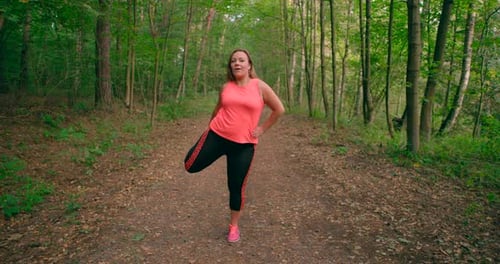Caucasian women in sportswear stretching legs and exercising in the forest trail.