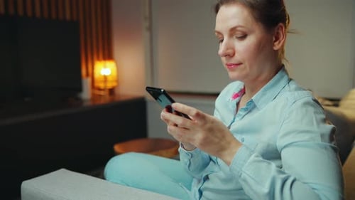 Eine Frau schreibt bequem zu Hause in entspannter Atmosphäre eine SMS auf ihrem Smartphone