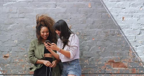 Two Friends Laughing at Phone on Urban Wall
