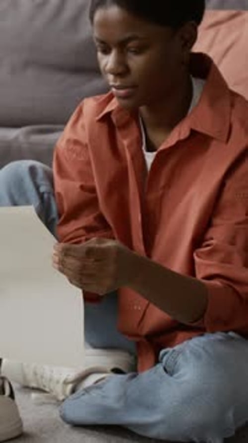 Vertical d'une jeune femme noire étudiant les instructions d'assemblage de tables à la maison