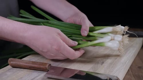 Fresh spring onions are sorted by Caucasian chef onto wooden chopping block