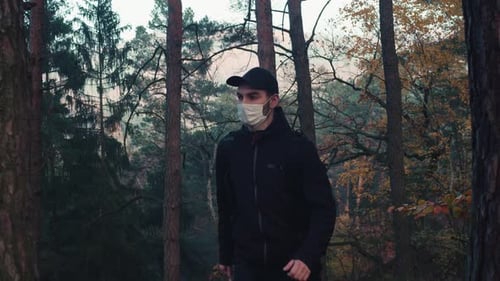 Caucasian man walking in forest with medical face mask, life after covid pandemic, middle shot side