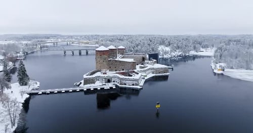 Drone approaching the snowy Olavinlinna castle, gloomy, winter day in Finland