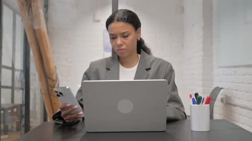 Woman Using Cellphone While Working on Laptop