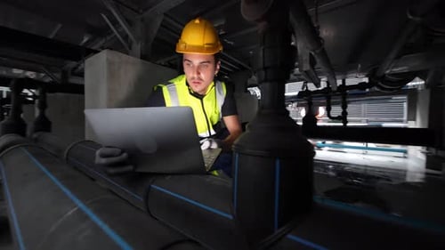 Worker engaged in maintenance activity under industrial equipment in a facility