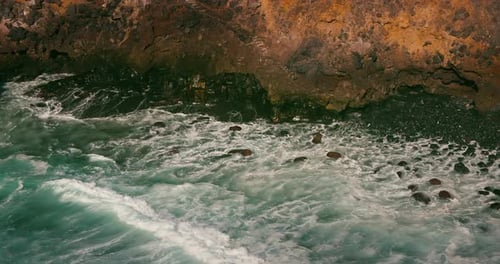 Ocean Waves Crashing Against Big Stones on Black Sandy Beach in Slowmotion Closeup Sea Water Foam
