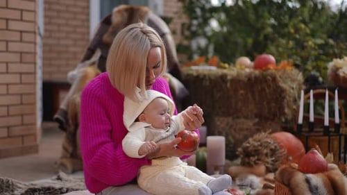 Blonde Woman Sits with Baby Surrounded by Pumpkins