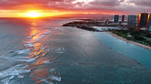 Wide waves roll to the shore at sunset. Beautiful orange sun in the sky at backdrop. Coast of Hawaii
