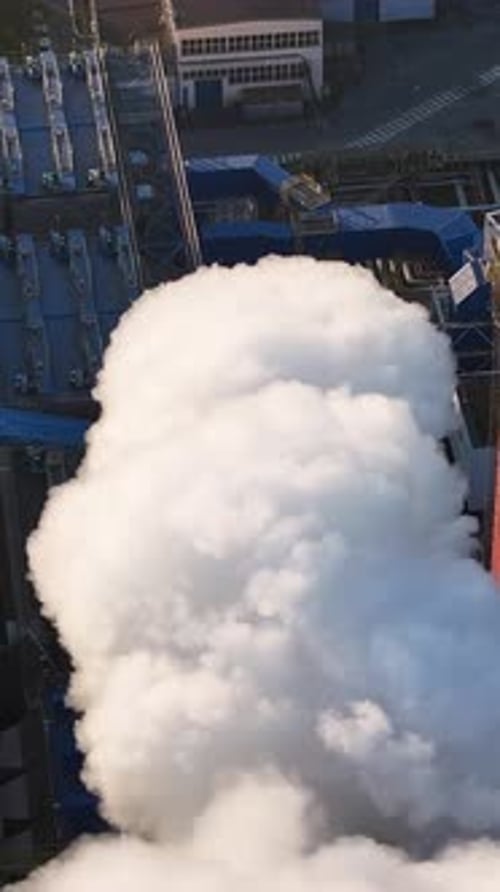 Steam billows from industrial chimney in a factory setting