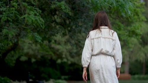 Unrecognizable Beautiful Young Woman in Long Dress Walks Through City Park Back View
