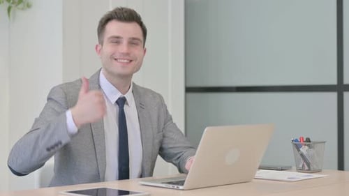 Man working at laptop in office gives thumbs up