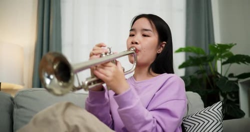 Young Adult Practices Trumpet on Couch Indoors