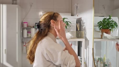 Woman Applies Facial Lotion in Bright Bathroom