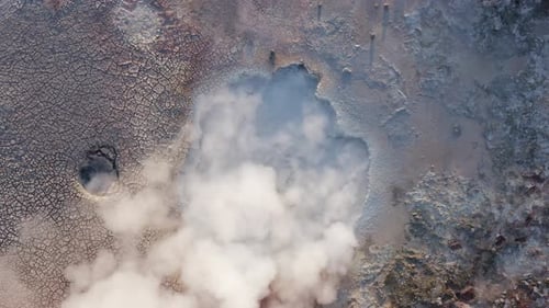 Top down aerial at boiling mud pool creating toxic gas, cracked surface