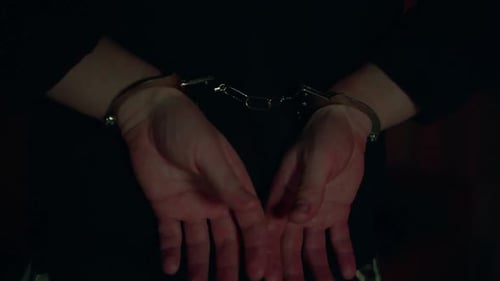 Arrested man's hands cuffed behind his back. Flashing blue and red, close-up.
