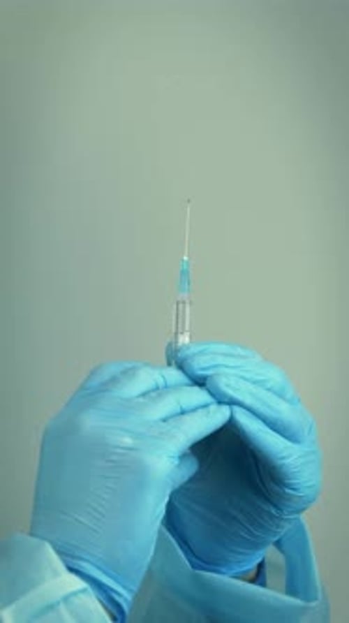 Close up of hands in medical protective gloves holding syringe. Vertical video