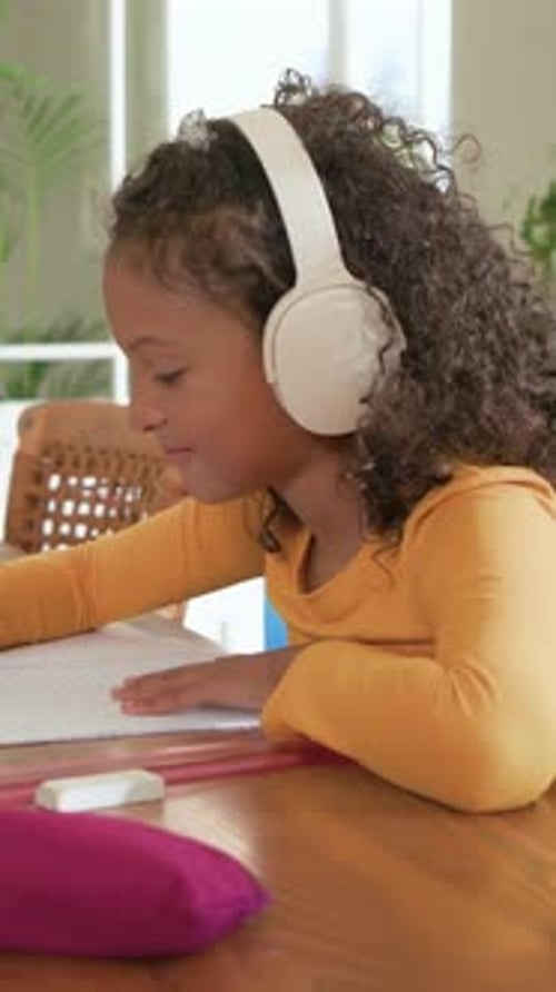 Vertical video: Listening after headset cue girl leaning over notebook at table wearing mustard top