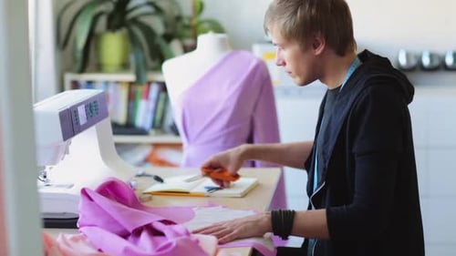 Young Man Cutting Pink Fabric in His Workshop